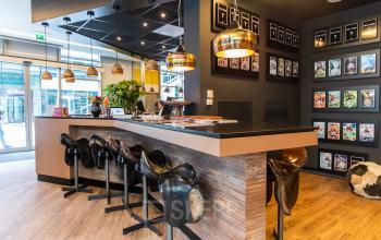 Moderne kantoorruimte met opvallende zadelstoelen aan een hoge tafel, decoratieve verlichting en kunst aan de muren, gelegen in kantoorpand aan Claude Debussylaan in Amsterdam Zuidas, geschikt voor kantoorruimte huren.