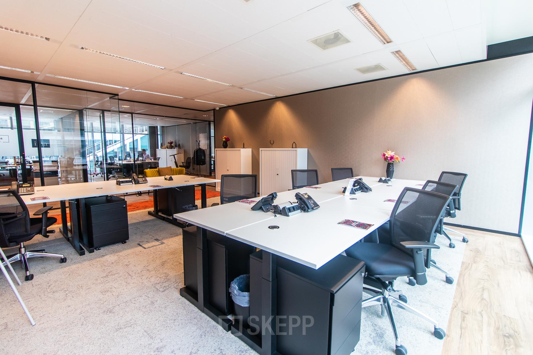 Moderne kantoorruimte aan Claude Debussylaan 7-29 in Amsterdam Zuidas, met meerdere bureaus, stoelen en glazen wanden. Ideaal voor zakelijke activiteiten en vergaderingen. Kantoorruimte huren mogelijk.