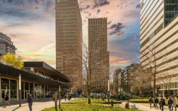 Kantoorpanden aan Gustav Mahlerplein 109-115 in Amsterdam Zuidas, bij zonsondergang, mensen lopen rond en genieten van het parkachtig gebied.