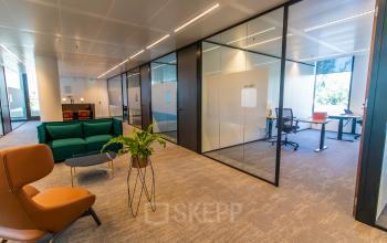 Kantoorruimte huren aan de Gustav Mahlerlaan 1212, Amsterdam Zuidas. Modern ingericht met glazen wanden, een loungeruimte met groene banken en een vergaderruimte.