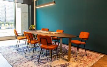 Vergaderruimte in modern kantoorpand Gustav Mahlerlaan 1212, Amsterdam Zuidas, met lange tafel, zes oranje stoelen en een tapijt.