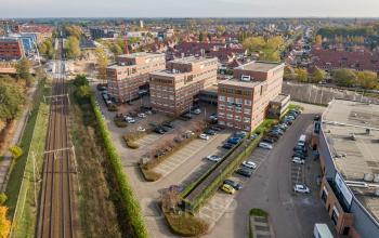 Luchtfoto van het kantoorpand aan Het Rietveld 55-59 in Apeldoorn, omgeven door parkeerplaatsen en nabij het spoor. Ideaal voor wie een kantoorruimte wil huren.