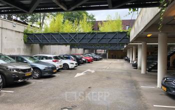 Ruime parkeerplaats bij kantoorpand aan Wapenrustlaan 11-31 in Apeldoorn, met meerdere geparkeerde auto's onder een open lucht structuur.