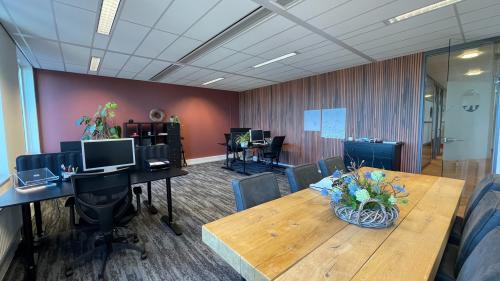 Kantoorruimte huren in Apeldoorn aan de Wapenrustlaan 11-31 met moderne inrichting, inclusief houten tafel en werkplekken met computerstations tegen een warme muur.