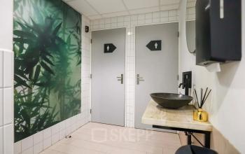Toiletruimte in kantoorpand met moderne elementen en natuurlijke decoratie op de muur, gelegen op Prins Willem-Alexanderlaan 301 in Apeldoorn.