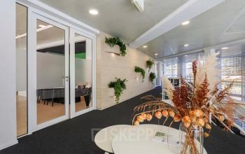 Binnenkant van een kantoorpand op Prins Willem-Alexanderlaan 301 in Apeldoorn, met groen decor en een glazen deur naar een vergaderruimte.