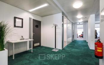 Kantoorruimte te huur aan Prins Willem-Alexanderlaan 301 in Apeldoorn, met groen tapijt en glazen wanden. De ruimte is voorzien van enkele meubels zoals een tafel en een kapstok.