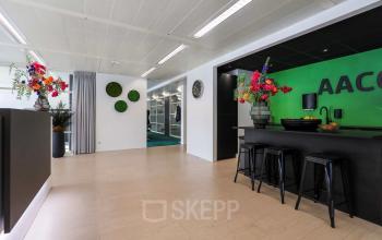 Kantoorruimte in Apeldoorn op Prins Willem-Alexanderlaan 301 met moderne inrichting, inclusief kleurrijke bloemen, enkele krukken en een open vloerplan voor kantoor activiteiten. Ideaal voor huren.