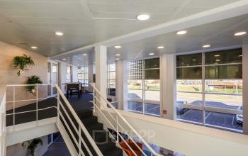 Moderne kantoorruimte huren op Prins Willem-Alexanderlaan 301, Apeldoorn, met ruime ramen en strakke inrichting op de verdieping via een centrale trap bereikbaar.