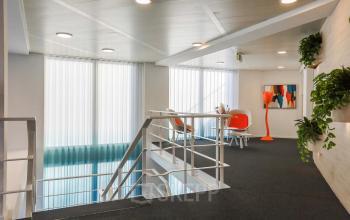 Kantoorruimte huren in Apeldoorn op Prins Willem-Alexanderlaan 301 met moderne witte muren, grote ramen en een trap met decoratieve planten.