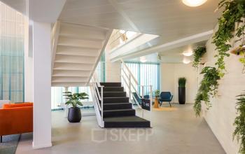 Moderne kantoorruimte huren in Apeldoorn met stijlvolle inrichting, inclusief open trap, planten en zitgedeelte. Lichte ruimte geschikt voor ontvangst en ontspanning.