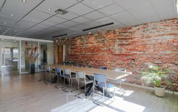 Kantoorruimte aan de Prins Willem-Alexanderlaan 401, Apeldoorn, met lange tafel en stoelen naast een bakstenen muur.