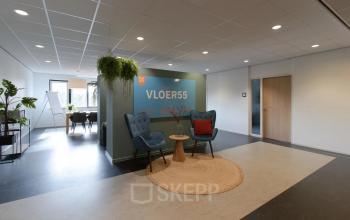 Kantoorinterieur met een zitruimte en een vergadertafel op de achtergrond, geschikt voor kantoorruimte huren in Apeldoorn.