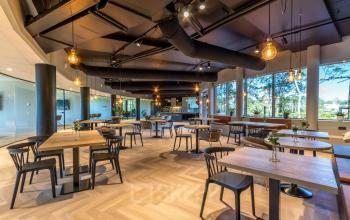 Ruime en moderne kantoorruimte in Apeldoorn met houten vloer, tafels en stoelen, grote ramen en stijlvolle verlichting. Ideaal voor bedrijven die kantoorruimte willen huren op Landdrostlaan 51.