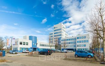 Exterieur van het kantoorpand op Prins Willem Alexanderlaan 701, Apeldoorn, met parkeerplaatsen aan de voorzijde en een blauwe lucht. Perfect voor kantoorruimte huren.