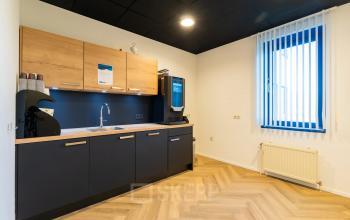 Een moderne pantry met houten kasten, een koffiezetapparaat en een spoelbak in een kantoorpand op Prins Willem Alexanderlaan 701, Apeldoorn. Perfect voor wie kantoorruimte wil huren.