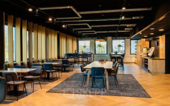 Moderne kantoorruimte met houten vloer, meerdere tafels en stoelen in een open werkopstelling op Prins Willem Alexanderlaan 701, Apeldoorn. Beschikbaar voor kantoorruimte huren.