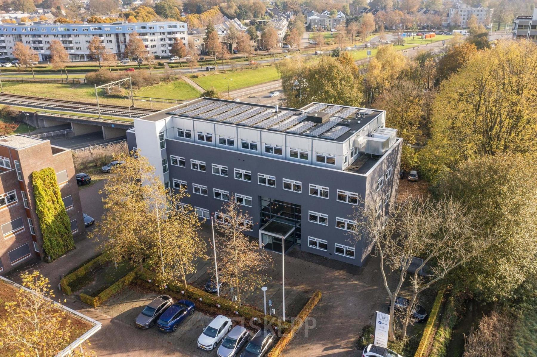 Luchtfoto van het kantoorpand Waterloseweg 7a, Apeldoorn, omgeven door bomen en een parkeerplaats met auto's. Ideale locatie voor kantoorruimte huren.