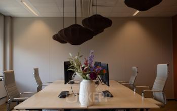 Moderne kantoorruimte huren in Apeldoorn met stijlvolle vergadertafel, comfortabele bureaustoelen en opvallende hanglampen. Groot bloemstuk op tafel, geschikt voor creatieve bijeenkomsten.
