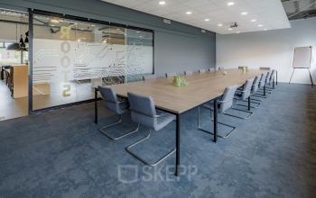 Kantoorruimte huren op Oude Apeldoornseweg 41-45 in Apeldoorn met een moderne vergaderruimte, lange tafel, comfortabele stoelen en glazen deur met opdruk. Ideaal kantoorpand voor vergaderingen.