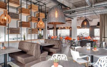 Moderne kantoorruimte huren aan Oude Apeldoornseweg 41-45, Apeldoorn. Ruim interieur met gezellige zithoeken, houten accenten en hanglampen. Ideaal voor ontspannen werkoverleg en creatieve brainstormsessies.