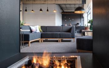 Moderne kantoorruimte huren op Oude Apeldoornseweg 41-45, Apeldoorn. Gemeubileerde lounge met comfortabele banken en sfeervolle verlichting. Personen voeren zakelijke gesprekken uit.
