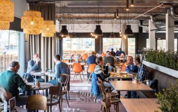 Gezellige kantoorkantine in kantoorpand op Oude Apeldoornseweg 41, Apeldoorn. Mensen lunchen aan verschillende tafels onder sfeervolle verlichting.