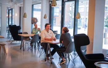 Ruime en lichte kantoorruimte te huur op Roggestraat 111, Apeldoorn, met moderne meubels en personen in zakelijke gesprekken aan tafels.