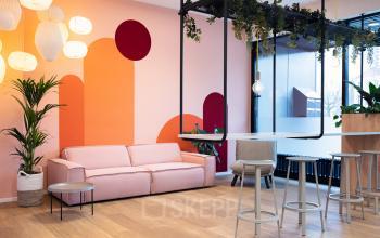 Moderne kantoorlounge in Arnhem Centrum aan de Jansbuitensingel 30, voorzien van een comfortabele roze bank, stijlvolle sta-tafels en speelse kleuraccenten.