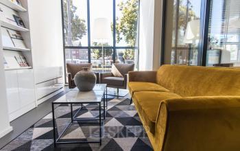 Een moderne en lichte kantoorruimte huren aan de Jansbuitensingel 7 in Arnhem Centrum, met stijlvolle meubels zoals een gele bank en glazen wand voor uitzicht over de stad.