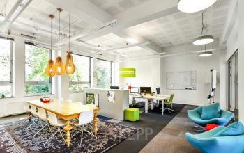 Moderne kantoorruimte huren aan Jansbuitensingel 7 in Arnhem Centrum, met veel natuurlijke lichtinval, kleurrijke meubels en aparte werkplekken binnen een open indeling.