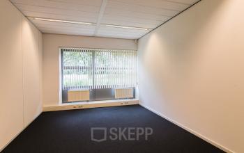 Lege kantoorruimte met grote ramen en een donkere vloerbedekking gelegen in kantoorpand Meander 251, Arnhem IJsseloord, ideaal om te huren.