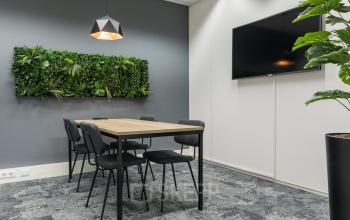 Kantoorruimte huren in kantoorpand op Delta 1, Arnhem IJsseloord. Moderne vergaderruimte met plantenwand, houten tafel, zes stoelen en grote monitor. Grijs vloerbedekking en zachte verlichting voor een professionele uitstraling.