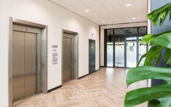 Entree van het kantoorpand op Delta 1, Arnhem IJsseloord, met moderne liftdeuren en een stijlvolle houten vloer. Ideaal voor wie kantoorruimte wil huren in een professionele omgeving.