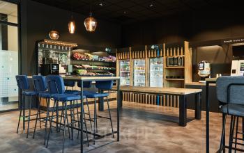 Kantoorpand op Delta 1, Arnhem IJsseloord met een moderne pantry. Er zijn hoge stoelen en tafels, een koffieautomaat en een selectie snacks en drankjes beschikbaar.