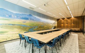 Kantoorruimte huren in Arnhem IJsseloord: ruime vergaderruimte met houten tafels, blauwe stoelen en een muurprint met natuuruitzicht bij Delta 1.