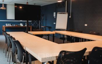 Vergaderruimte in Arnhem IJsseloord met een U-vormige opstelling van houten tafels, zwarte stoelen en een groot scherm. Kantoorruimte huren in kantoorpand op Vlamoven 34, uitgerust voor zakelijke bijeenkomsten.