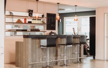 Moderne kantoorruimte met een stijlvolle bar met hoge stoelen en sfeervolle verlichting, ideaal voor informeel overleg en ontspanning. Perfect om een kantoorruimte te huren op Vlamoven 34 in Arnhem IJsseloord.