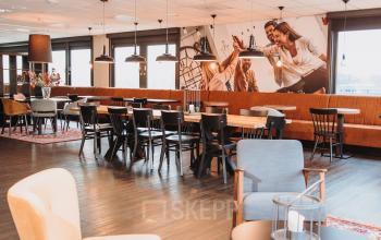 Modern ingerichte kantoorruimte met lange tafels en zitmogelijkheden in kantoorpand aan de Vlamoven 34, Arnhem IJsseloord. Ideaal om te gebruiken voor vergaderingen of informeel overleg.