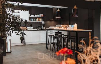 Moderne pantry in een kantoorpand op Vlamoven 34, Arnhem IJsseloord. Ruimte met strak design, voorzien van een hoog tafelblad en krukken, ideaal voor kantoorruimte huren.