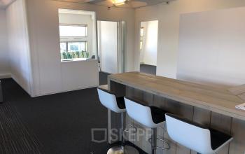 Kantoorruimte huren aan de Simon Stevinweg 27 in Arnhem Oost, met een hoge tafel en drie witte barkrukken, naast een vergaderruimte.