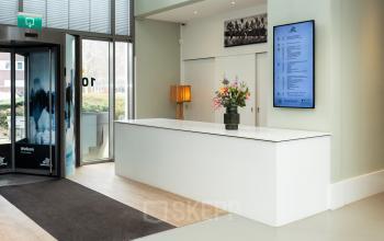 Entree van kantoorpand aan Mr D.U. Stikkerstraat 10 in Arnhem Zuid, moderne balie met bloemenvaas, scherm met informatie en glazen ingang.