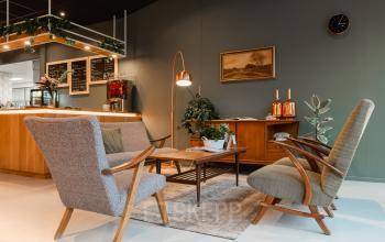 Gezellige loungehoek in kantoor op Mr D.U. Stikkerstraat 10, Arnhem Zuid, met comfortabele stoelen, een houten tafel en groene planten.