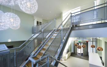 Moderne entreehal met metalen trap en opvallende hanglampen in een kantoorpand aan de Mr D.U. Stikkerstraat 10, Arnhem Zuid.