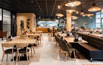 Moderne ingerichte kantoorpand aan Mr D.U. Stikkerstraat 10 in Arnhem Zuid, met houten tafels en stoelen, hanglampen, en een open keuken.