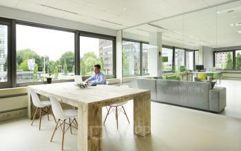 Kantoorruimte huren op Mr D.U. Stikkerstraat 10 in Arnhem Zuid, Arnhem met een houten tafel, witte stoelen, glazen wanden, en een man die op zijn laptop werkt.