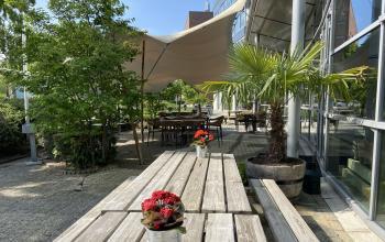 Buitenterrein van het kantoorpand op Mr D.U. Stikkerstraat 10 in Arnhem Zuid met tafels, stoelen en parasols voor informeel gebruik dankzij de groene omgeving en moderne uitstraling.