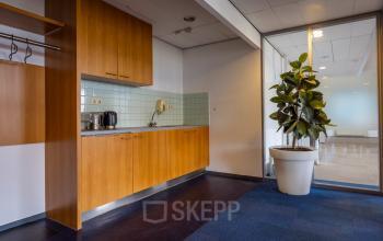 Kantoorruimte huren op Kronenburgsingel 525 in Arnhem Zuid, met een kleine kitchenette en een grote plant naast een glazen wand.
