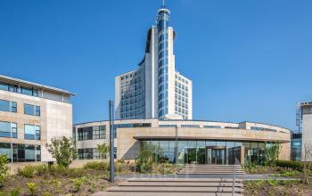 Exterieur van het kantoorpand gelegen op Rijksweg-West 2, Arnhem Zuid. Modern design met glazen gevels en een centraal hoog gebouw. Voorzijde met trappen en groenvoorziening.