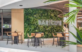 Moderne kantoorruimte in Arnhem Zuid, Rijksweg-West 2, ingericht met hoge tafels en stoelen, voorzien van een groene plantenwand en heldere verlichting.